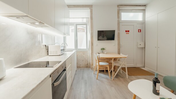 Een moderne keuken met witte kasten, een magnetron en een eethoek met tafel en stoelen.
