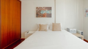 Una habitación de hotel con una cama grande, un armario de madera, una mesita de noche y una obra de arte colgada en la pared.