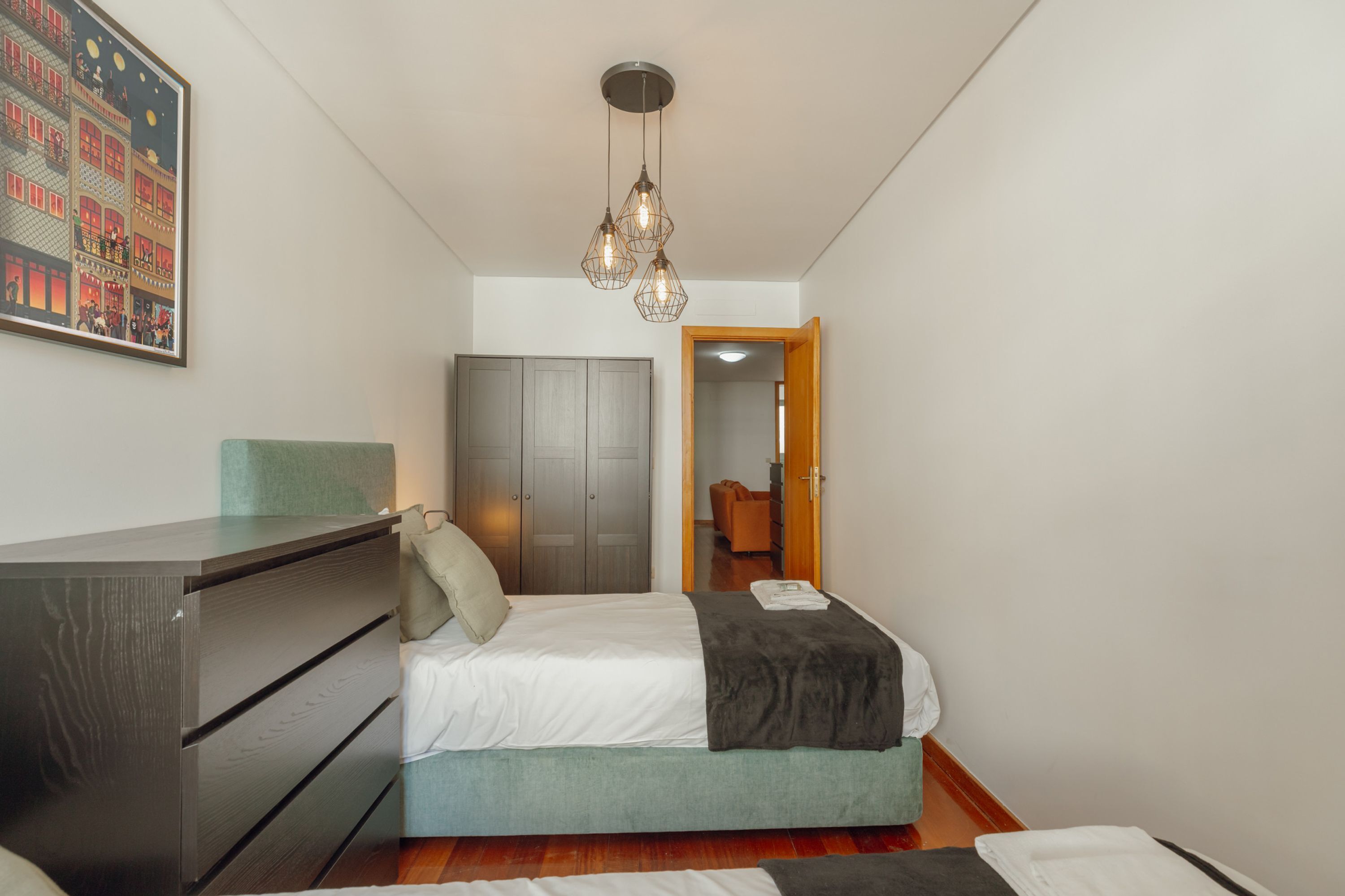 A bedroom with a bed, dresser, wardrobe, and a hanging light fixture.