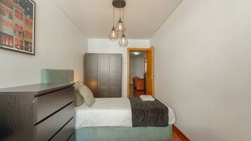A bedroom with a bed, dresser, wardrobe, and a hanging light fixture.
