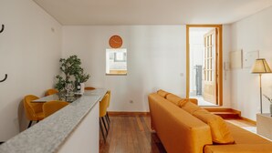 Una sala de estar moderna con sofá, mesa de comedor, sillas y una cocina visible a través de un ventanal.