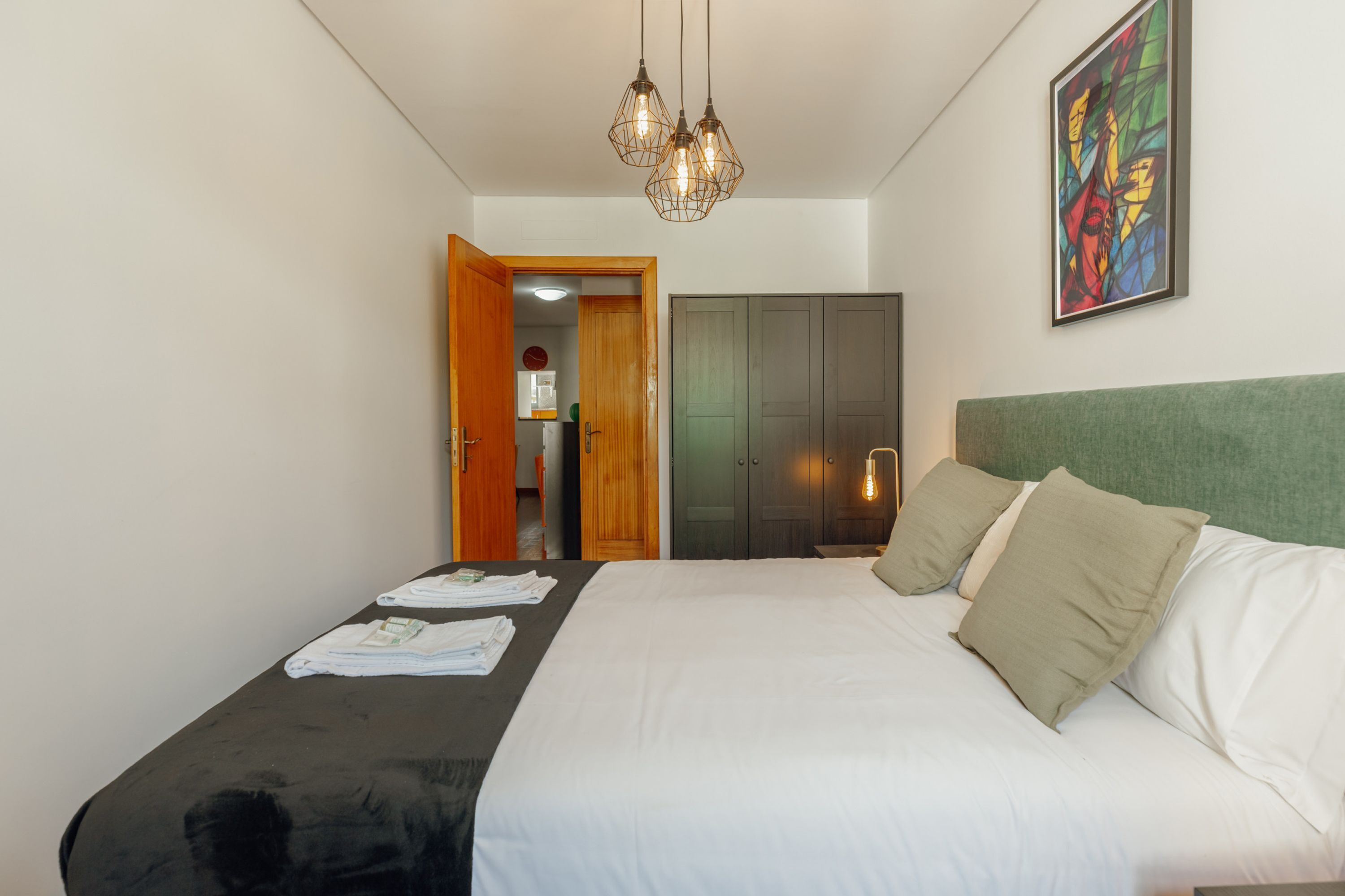 A bedroom with a large bed, a wooden door, a wardrobe, and a painting on the wall.