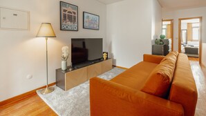 Una sala de estar moderna con un sofá grande color naranja, un televisor de pantalla plana sobre un mueble de madera, una lámpara de pie y cuadros enmarcados en la pared.