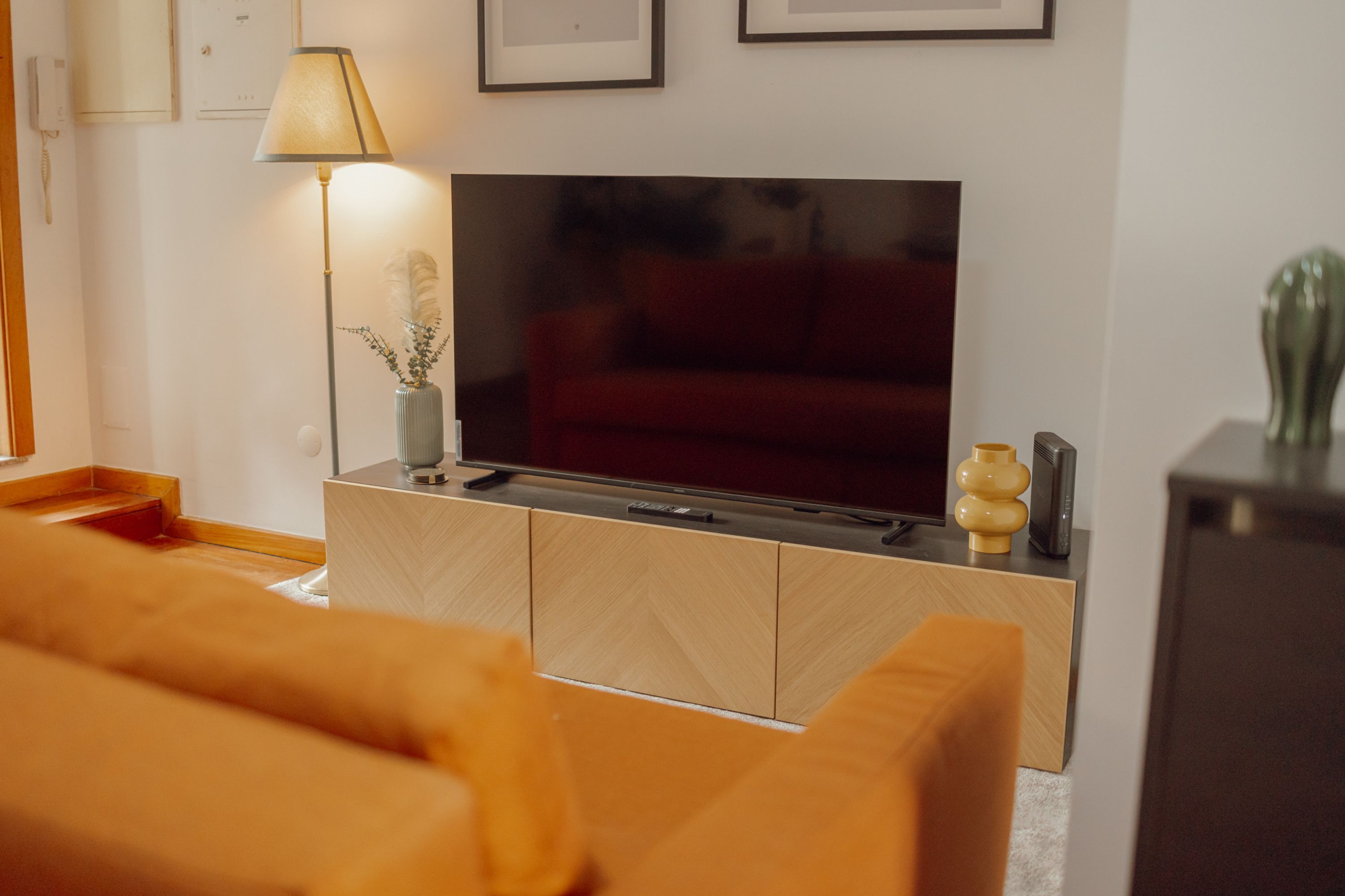 A modern living room with a flat-screen TV on a wooden cabinet, a lamp, and a sofa.
