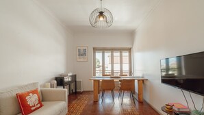 A living room with a sofa, a dining table, chairs, a TV, and a patterned rug. - Santa Catarina Flat 2BD With Balcony by Vacationy (Porto)