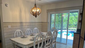 A dining area with a white table and chairs, a chandelier, and a view of a swimming pool through glass doors. - Near Clearwater Tampa Serene 3-bedroom house with Hot Tub in charming Oldsmar (Oldsmar)