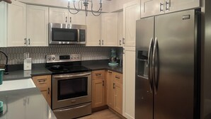 A modern kitchen with stainless steel appliances, wooden cabinets, and a chandelier. - Near Clearwater Tampa Serene 3-bedroom house with Hot Tub in charming Oldsmar (Oldsmar)