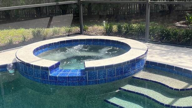 A swimming pool with a blue-tiled hot tub area. - Near Clearwater Tampa Serene 3-bedroom house with Hot Tub in charming Oldsmar (Oldsmar)