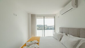 A hotel room with a bed, a window with a view, and an air conditioning unit.