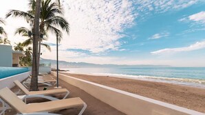 A beachside hotel with sun loungers, palm trees, and a view of the ocean. - Beachfront Studio,  New & Cozy,   Stunning Ocean Views,  Prime Location (Puerto Vallarta)