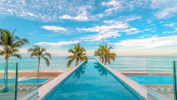 A infinity pool with a clear view of the ocean and palm trees. - Beachfront Studio,  New & Cozy,   Stunning Ocean Views,  Prime Location (Puerto Vallarta)