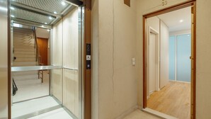 An elevator with a control panel, a wooden door, and a view into a room with a wooden floor and a door. - Bright Window Apartment by Vacationy (Porto)
