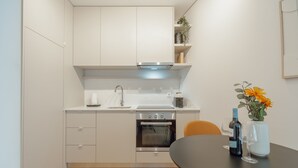 A modern kitchen with white cabinets, a built-in oven, a sink, and a dining area with a table. - Bright Window Apartment by Vacationy (Porto)