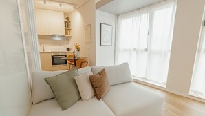 A modern living room with a sofa, a dining table, and a kitchen in the background. - Bright Window Apartment by Vacationy (Porto)