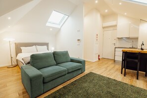 A modern, well-lit room with a green sofa, a small dining table, and a kitchen area. - Rooftop Constitui AO by Vacationy (Porto)
