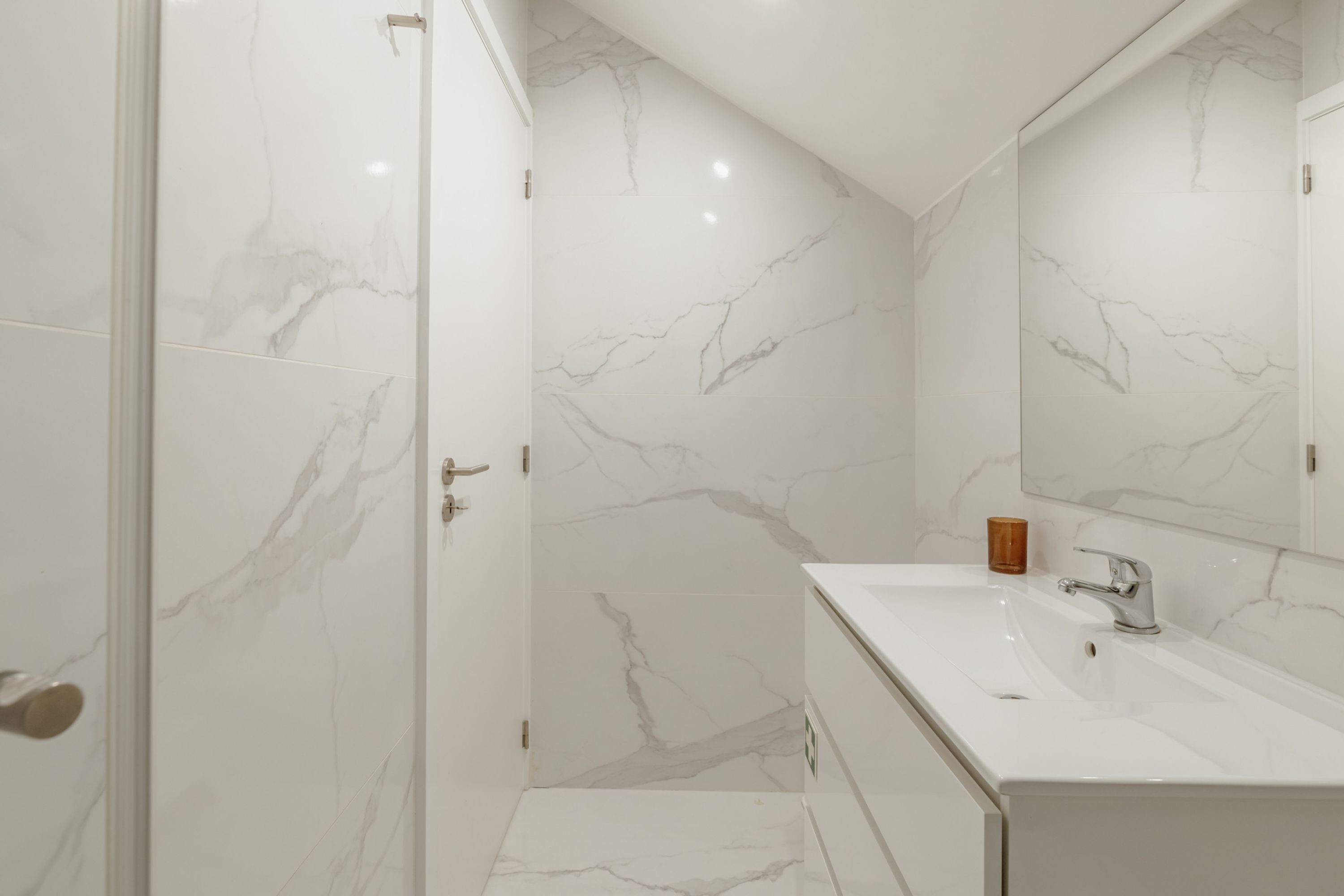 Un baño moderno con lavamanos de mármol blanco, un espejo grande y una cabina de ducha de vidrio.