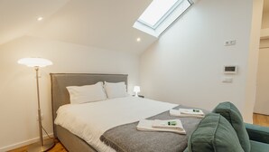 A modern hotel room with a large bed, a standing floor lamp, a green sofa, and a skylight. - Rooftop Constitui AO by Vacationy (Porto)
