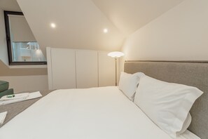 A neatly made bed with white linens, a bedside lamp, and a view of a room with a wardrobe and a mirror. - Rooftop Constitui AO by Vacationy (Porto)