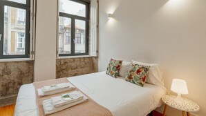 Une chambre d’hôtel avec un lit, une table ronde avec une lampe et une fenêtre donnant sur des immeubles.