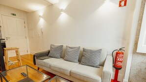Une pièce comprenant un canapé, une table basse en verre, un extincteur et un plancher en bois.