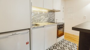 Une cuisine de taille réduite avec des meubles blancs, un pare-feu en marbre et un carrelage décoratif.