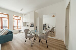 Una cocina moderna con armarios blancos, una mesa de comedor de vidrio y un sofá en una habitación luminosa con ventanas amplias.