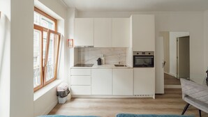 Moderni keittiö, jossa on valkoiset kaapit, sisäänrakennettu uuni ja ikkuna, jossa on sälekaihtimet.