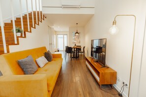 Un soggiorno moderno con scala in legno, un divano giallo brillante, un'area pranzo e un televisore su un supporto in legno.