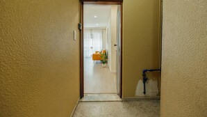 Un couloir avec une porte donnant sur une pièce où se trouvent un lit et une fenêtre.