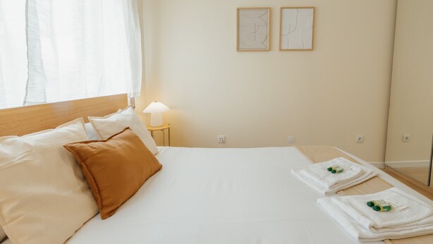 Une chambre d’hôtel avec un lit, des oreillers, une table de chevet avec une lampe, des serviettes et deux tableaux encadrés au mur.