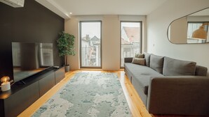 A modern living room with a flat-screen TV, a grey sofa, a wooden floor, and a large window. - Gaia Premium D Apartment by Vacationy (Vila Nova de Gaia)