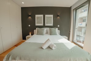 Quarto com cama, dois quadros na parede, mesa de cabeceira e janela.