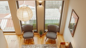 Een moderne kamer met een houten vloer, twee gestreepte stoelen, een klein plantje en een groot raam met uitzicht op een balkon.