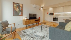 Een moderne woonkamer met een flatscreen televisie, een houten kast, een grijze bank en een kamerkleed met dessin.