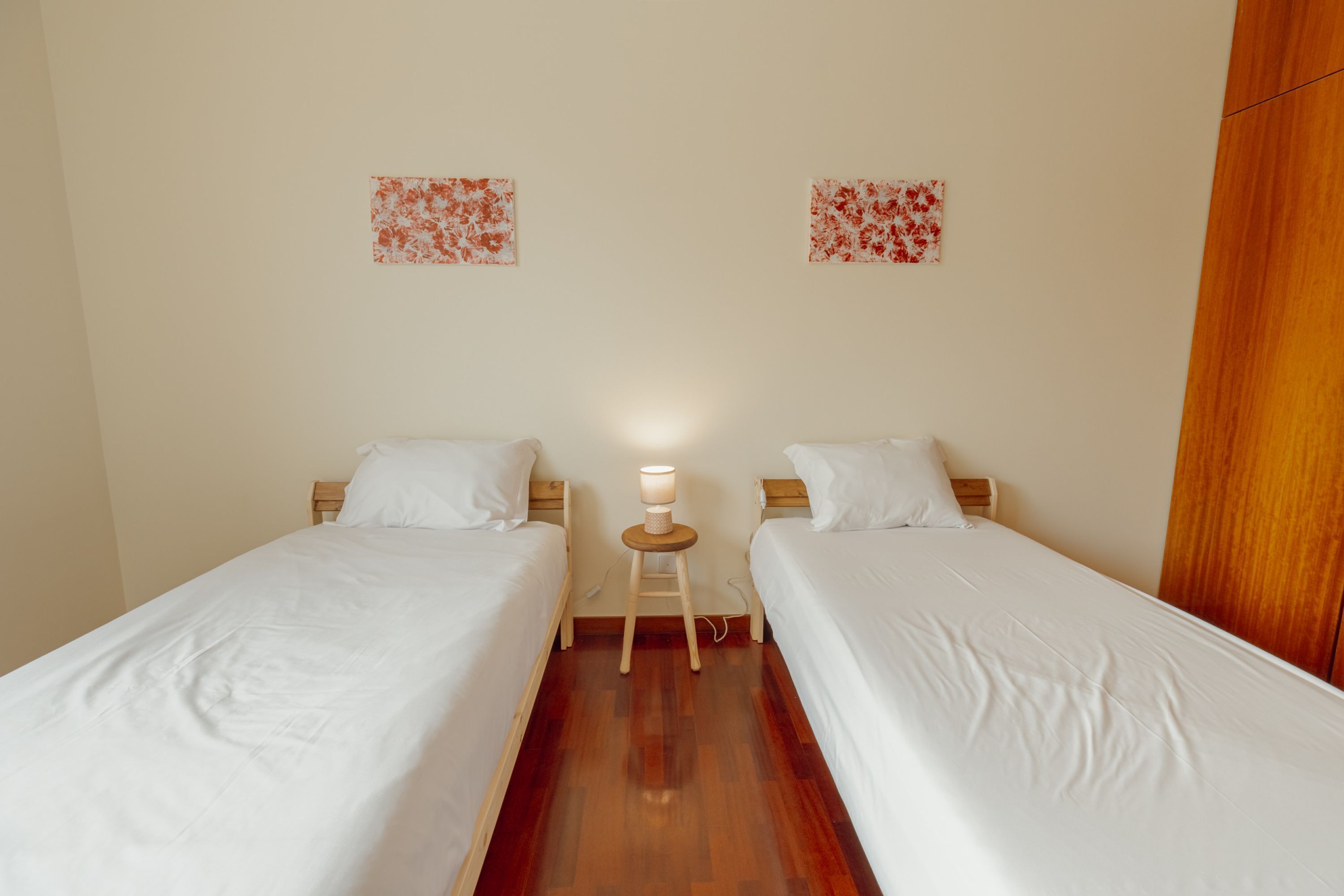 A twin room with two single beds, a small wooden nightstand with a lamp, and two wall-mounted floral artwork pieces.
