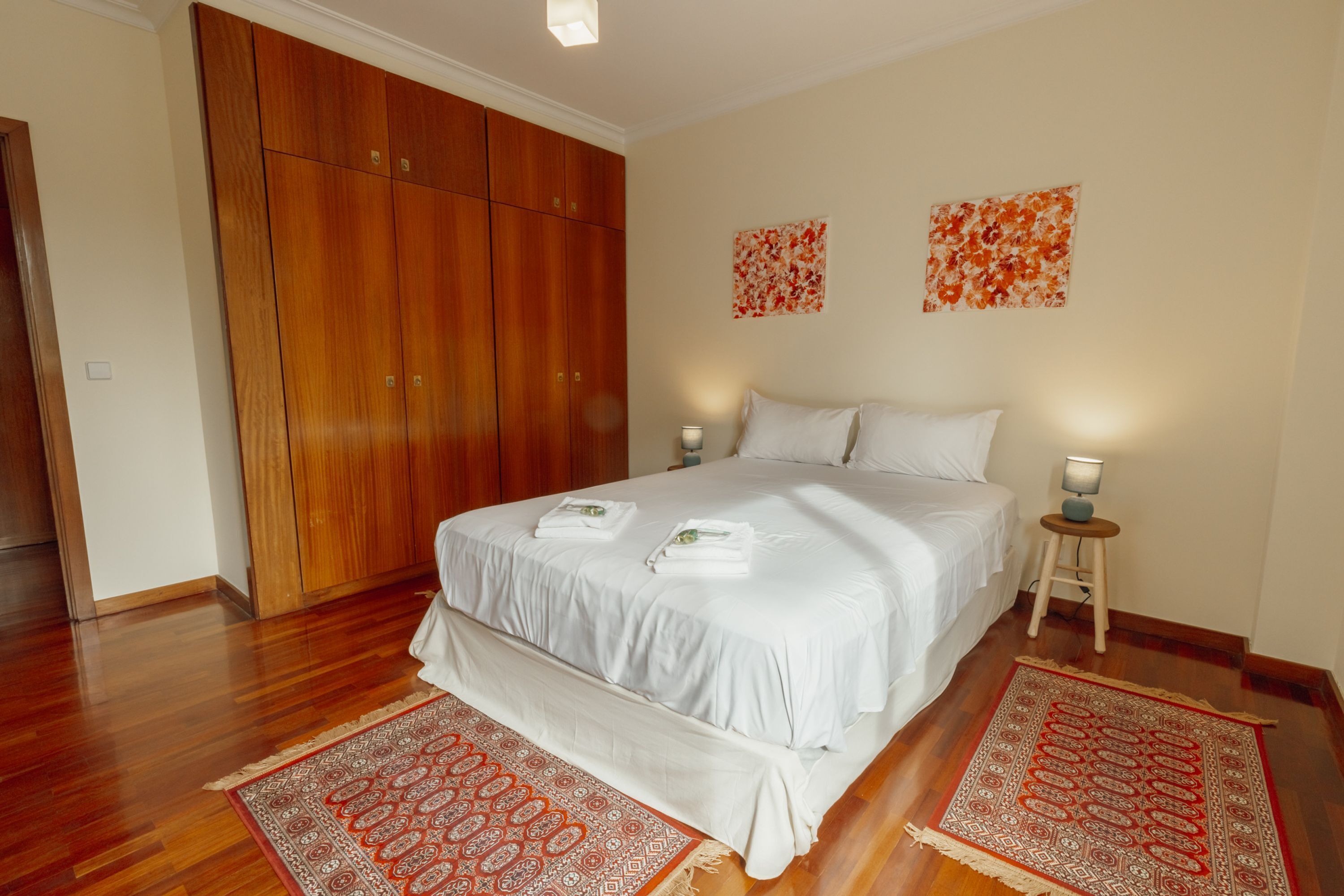 Een slaapkamer met een groot bed, een houten garderobe, twee wandlampen en twee tapijten met een patroon.