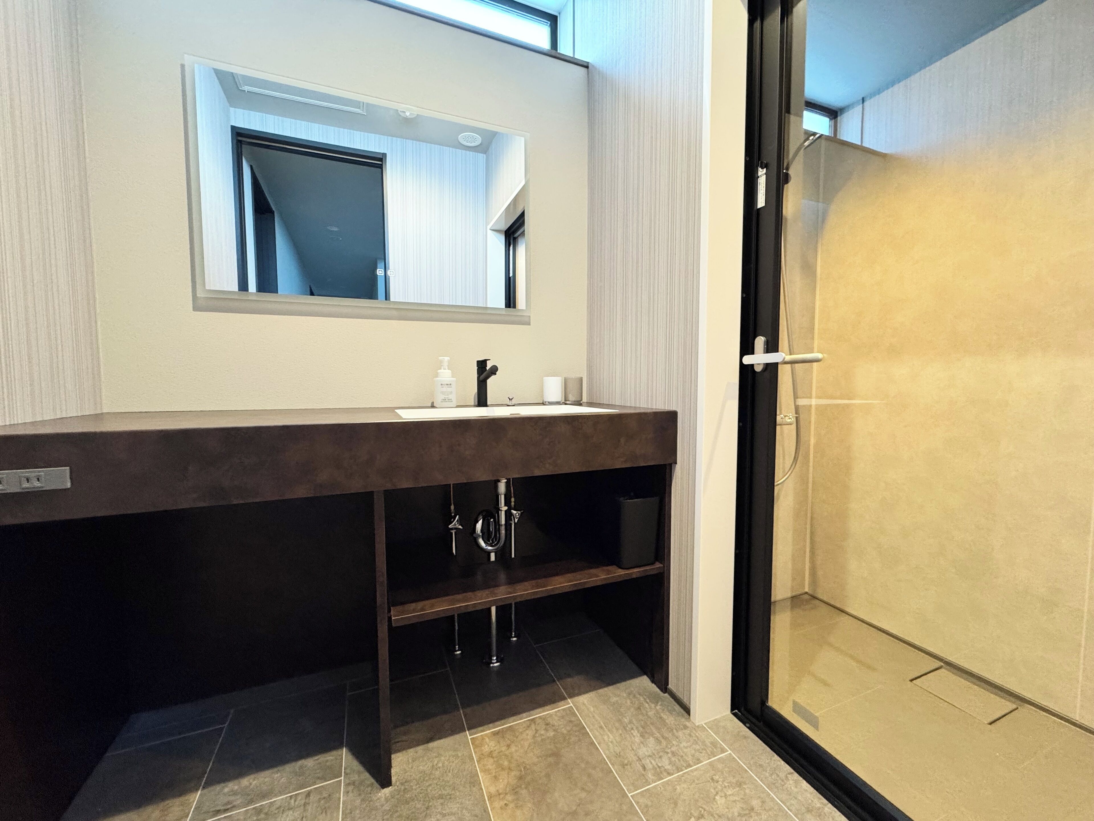 A modern bathroom with a dark vanity, a large mirror, and a glass-enclosed shower.