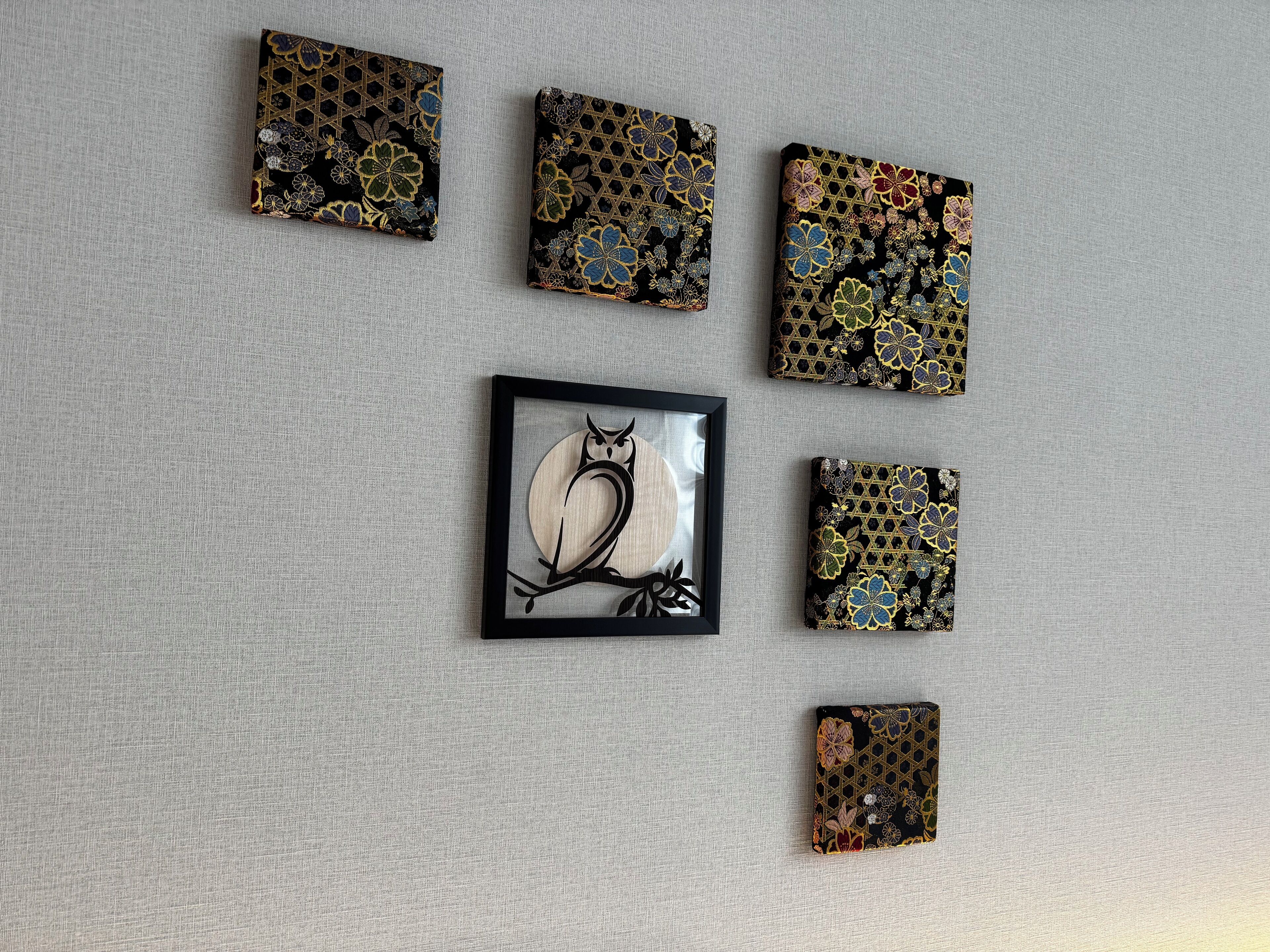 Six œuvres d’art de forme carrée, ornées de motifs floraux, sont disposées sur un mur à texture.