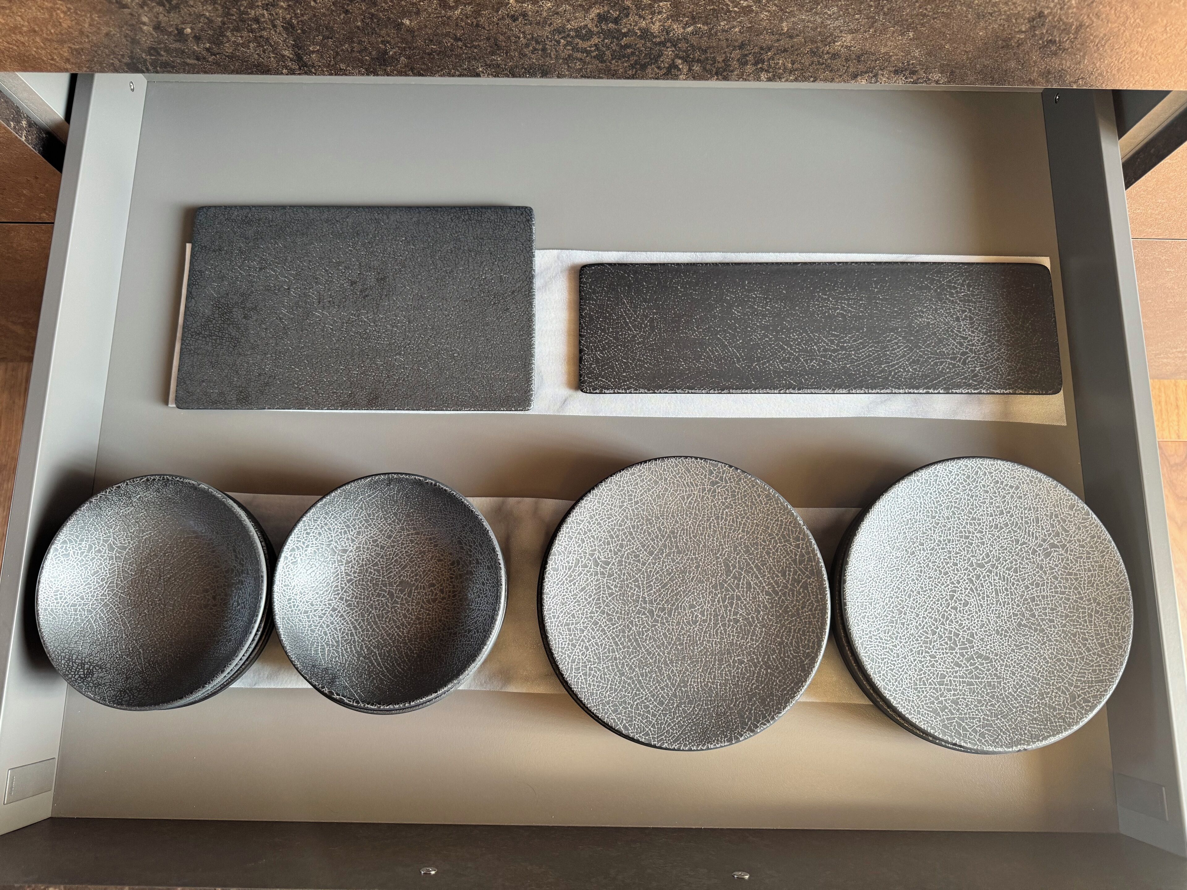 A drawer with various kitchenware items including plates and a rectangular tray.