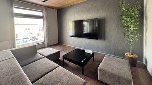 A modern living room with a flat-screen TV mounted on the wall, a wooden ceiling, and a large window with a view of parked cars outside. - The Villa Hotels -SAPPORO- (Sapporo)
