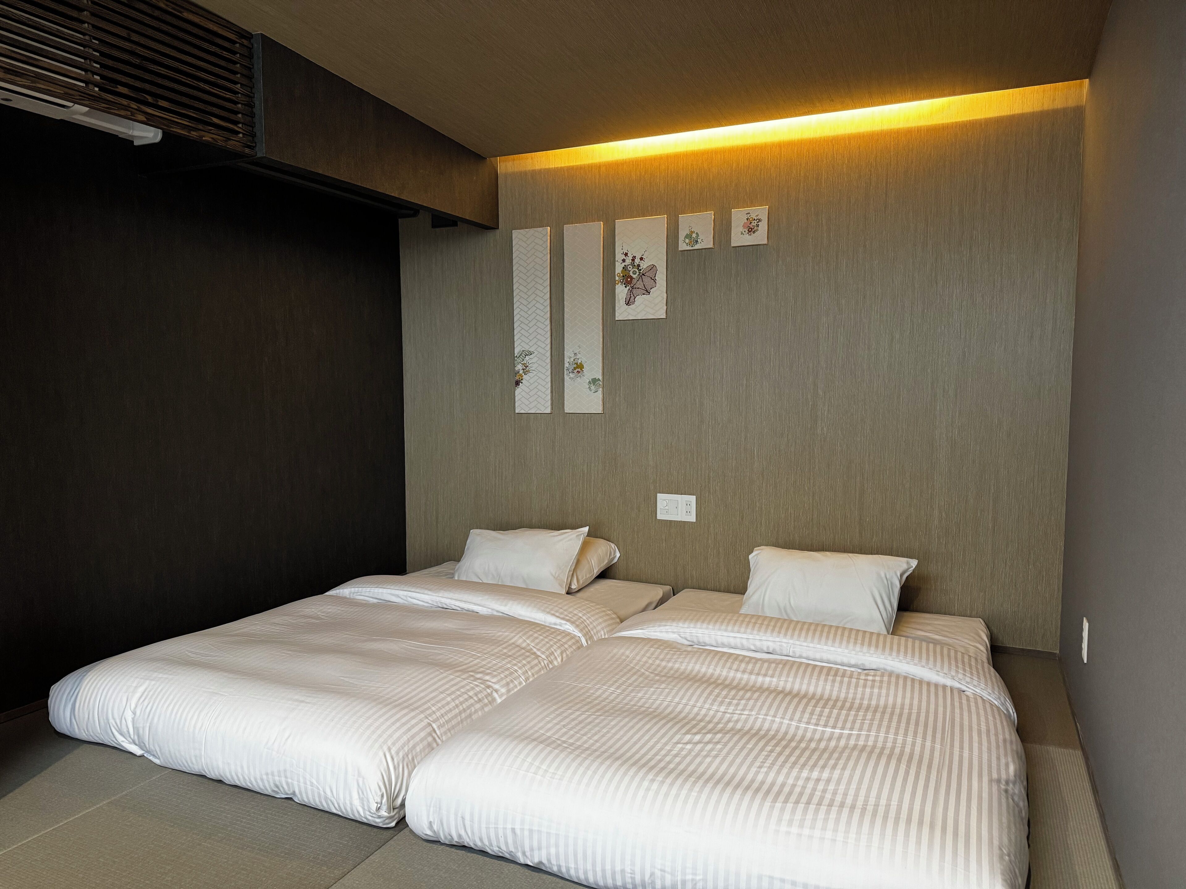 A modern bedroom with two beds, a wooden headboard, and wall-mounted artwork.