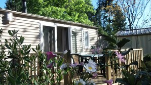 A wooden deck with a table and chairs, surrounded by various plants and flowers. - Gitotel 1-Bedroom Chalet for 2 People (ST JEAN DU GARD)