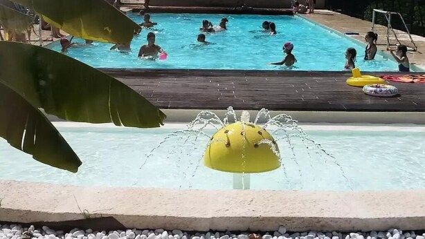 A swimming pool with people in the water, a water fountain, and a wooden deck. - Gitotel 1-Bedroom Chalet for 2 People (ST JEAN DU GARD)