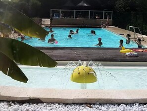 Una piscina con gente en el agua, una fuente y una cubierta de madera.