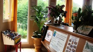 A reception area with a desk, potted plants, informational posters, and a window with curtains. - Gitotel 1-Bedroom Chalet for 2 People (ST JEAN DU GARD)