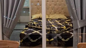 A bedroom with a tufted headboard, a patterned bedspread, and a small wooden table with a green object on it. - Fan Family Bromo Homestay (Ngadisari)