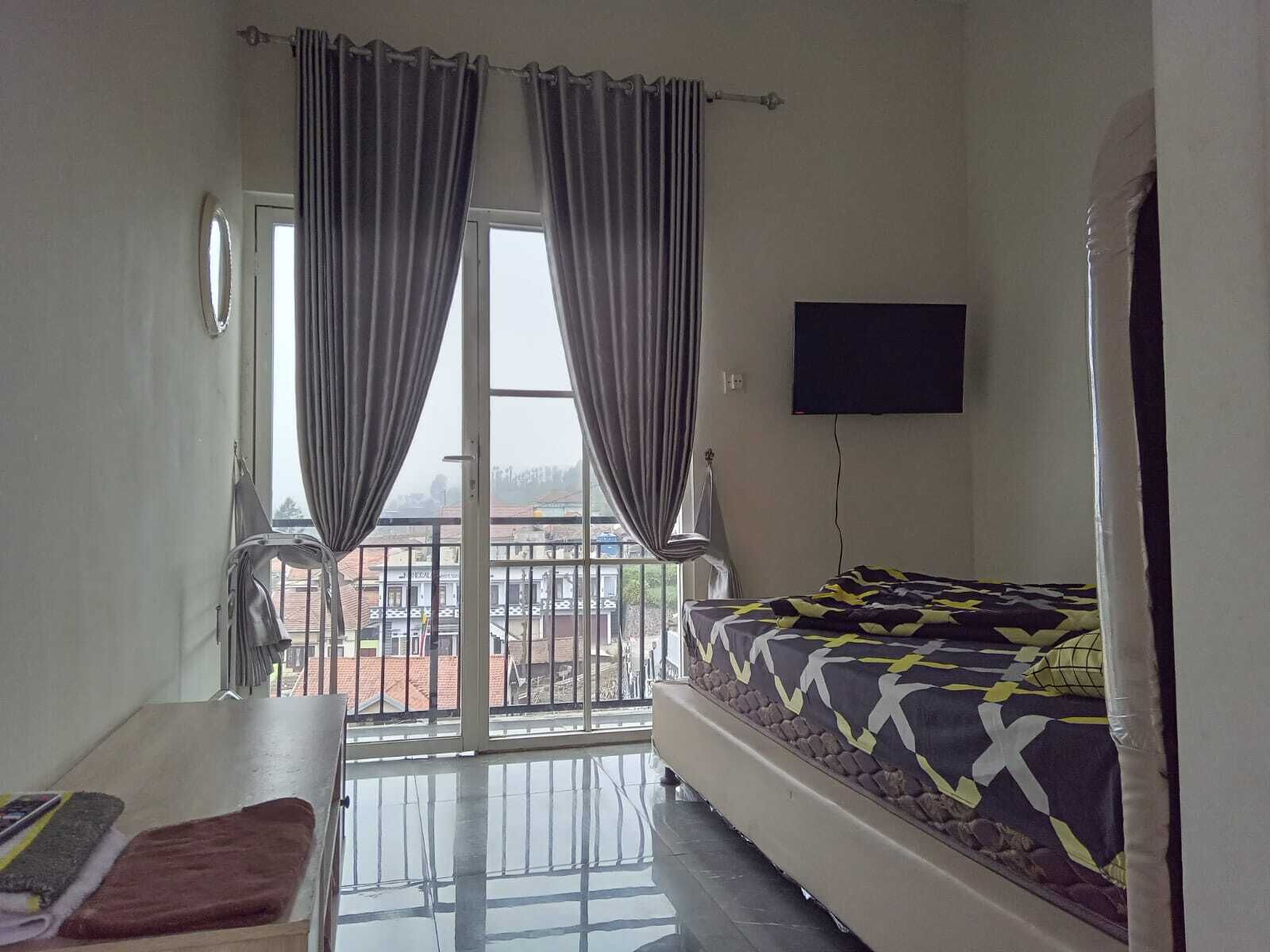 Una camera da letto con un letto, una TV fissata al muro e un balcone con tende.