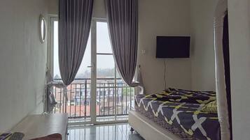 Una camera da letto con un letto, una TV fissata al muro e un balcone con tende.