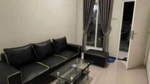 A modern living room with a black leather sofa, a glass coffee table, and a sliding glass door leading to a balcony. - Fan Family Bromo Homestay (Ngadisari)