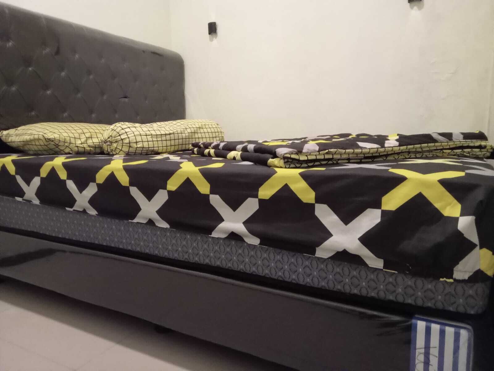 A bed with a black and yellow patterned bedspread, a grey headboard, and two pillows.